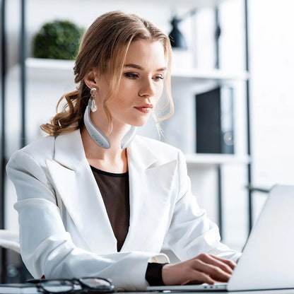 Woman using neck massager at desk with laptop, white blazer, office setting