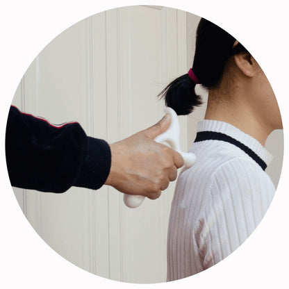 Hand using white massage tool on person's shoulder, home wellness device for muscle relief