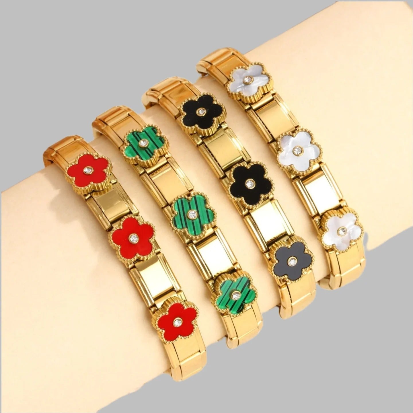 Gold flower bracelets with red, green, black, and white enamel petals and crystal centers, worn on wrist