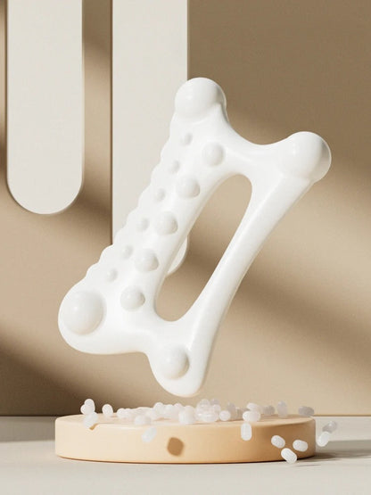 White ergonomic massage tool with textured nodules for muscle relief, displayed on beige stand with scattered beads